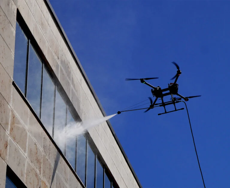 Cleaning drone spraying pure water at a high-rise glass façade with hose tether